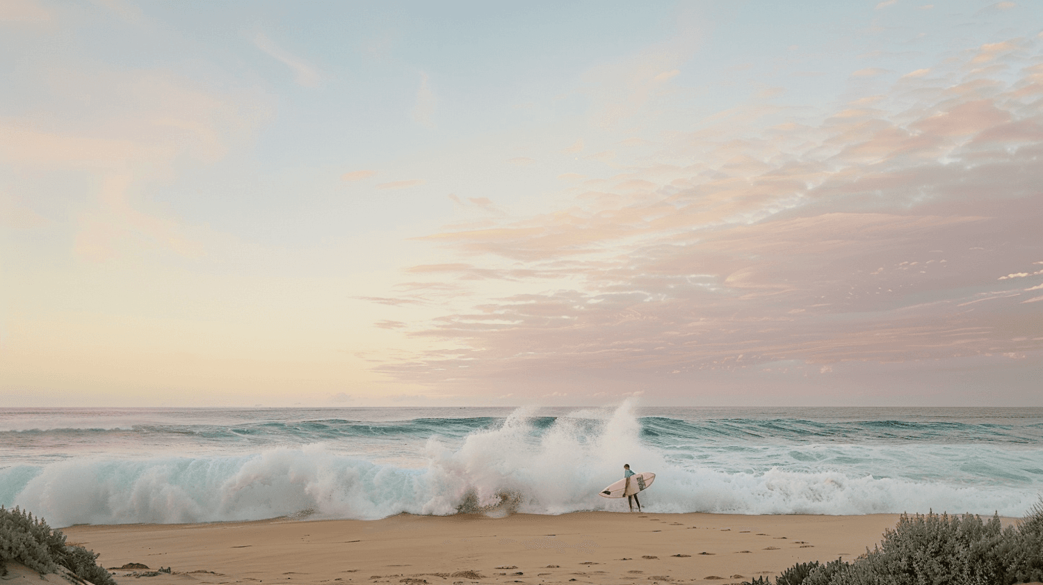 A surfer carrying a board along the shoreline as a wave breaks under a pastel sunrise sky